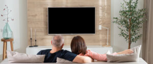 Couple watching TV mounted above fireplace, deciding between flat and tilt mount