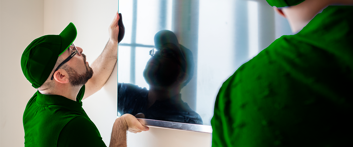 Professional technician in green uniform carefully mounting a flat screen TV on a white wall